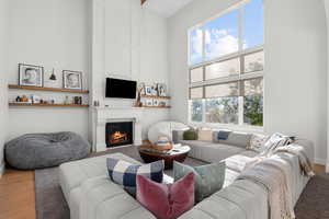 Living room with wood finished floors, a towering ceiling, plenty of natural light, and a fireplace