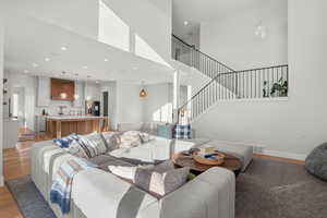 Living room with light wood-style floors, a towering ceiling, stairway, and recessed lighting