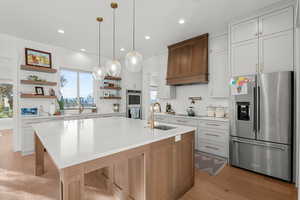 Kitchen featuring appliances with stainless steel finishes, white cabinets, a large island with sink, open shelves, and light stone counters