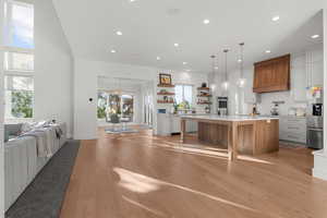 Kitchen with brown cabinets, open floor plan, pendant lighting, light wood finished floors, and tasteful backsplash