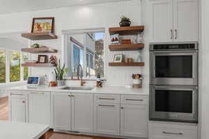 Kitchen featuring open shelves, stainless steel double oven, white cabinetry, and backsplash