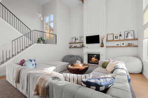 Living room with wood finished floors, a high ceiling, a fireplace, and stairway