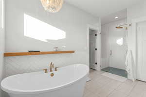 Bathroom featuring tile walls, a freestanding tub, a shower stall, light tile patterned floors, and a wainscoted wall