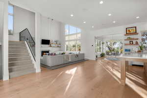 Living area featuring light wood-style floors, recessed lighting, a large fireplace, stairs, and a high ceiling