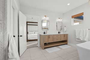 Ensuite bathroom with double vanity, light tile patterned flooring, a freestanding bath, and recessed lighting