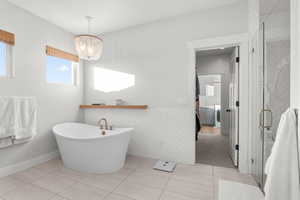 Ensuite bathroom featuring light tile patterned floors, tile walls, a freestanding bath, a stall shower, and wainscoting