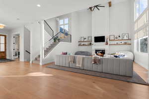 Living room with a lit fireplace, light wood-style flooring, plenty of natural light, a high ceiling, and recessed lighting