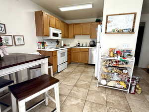 Kitchen with light countertops, white appliances, light tile patterned floors, and brown cabinetry