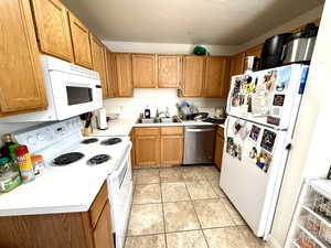 Kitchen featuring light countertops, white appliances, brown cabinets, and light tile patterned flooring