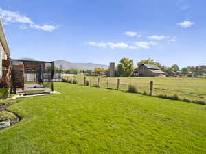 View of yard with a trampoline, a mountain view, a view of countryside, and a barn
