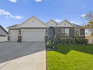 View of front facade featuring board and batten siding, a front yard, concrete driveway, a garage, and brick siding