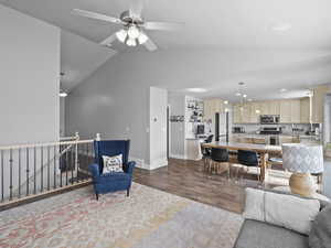 Living room featuring dark wood-style flooring, lofted ceiling, a chandelier, recessed lighting, and a ceiling fan