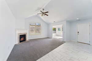 Unfurnished living room featuring light colored carpet, a tile fireplace, a ceiling fan, and high vaulted ceiling