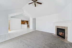 Unfurnished living room featuring a tiled fireplace, carpet, ceiling fan, high vaulted ceiling, and marble finish floors
