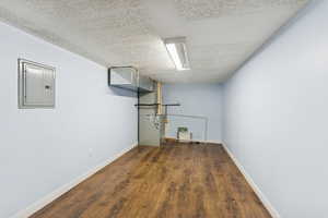 Finished basement with electric panel, dark wood-type flooring, a textured ceiling, and heating unit