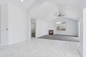 Unfurnished living room featuring lofted ceiling, a fireplace, light marble finish flooring, and a ceiling fan