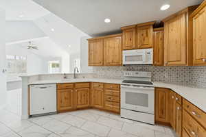 Kitchen featuring white appliances, vaulted ceiling, brown cabinetry, tasteful backsplash, and light stone countertops