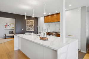 Kitchen featuring modern cabinets, decorative light fixtures, a large island with sink, premium stove, and light stone countertops