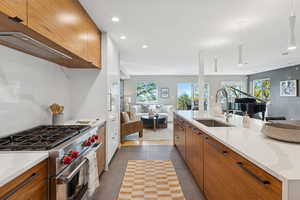 Kitchen featuring brown cabinetry, luxury stove, open floor plan, light stone countertops, and recessed lighting
