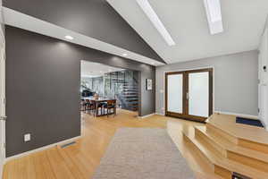 Foyer entrance with floating stairwayin background, French doors, vaulted ceiling, light wood finished floors, and a skylight.
