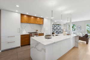 Kitchen featuring modern cabinets, brown cabinetry, decorative backsplash, light stone countertops, and open floor plan