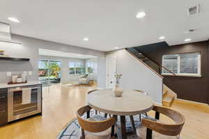 Dining area with light wood-style floors, stairway, recessed lighting, and beverage cooler