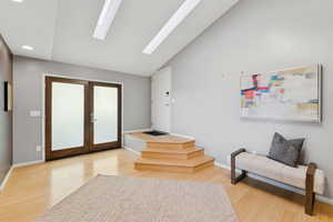 Foyer entrance featuring French doors, a skylight, light wood-style floors, lofted ceiling, and recessed lighting