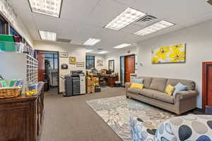 Living room with a desk, light colored carpet, and a paneled ceiling