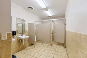 Bathroom featuring tile walls, wainscoting, light tile patterned floors, a stall shower, and a textured ceiling