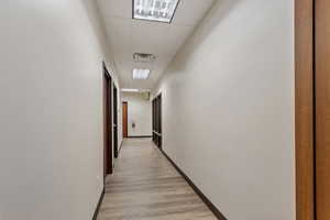 Corridor with a paneled ceiling and light wood-style flooring