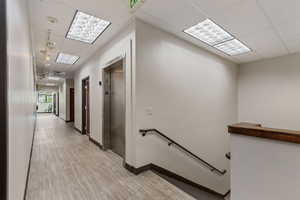Hall with a drop ceiling, an upstairs landing, elevator, and light wood-style flooring
