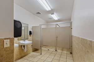 Bathroom with tile walls, a wainscoted wall, a shower stall, light tile patterned floors, and a textured ceiling