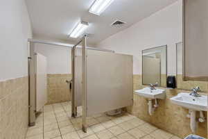 Full bath with tile walls, a stall shower, a wainscoted wall, and light tile patterned floors