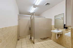 Bathroom featuring tile walls, a wainscoted wall, light tile patterned floors, and a shower stall