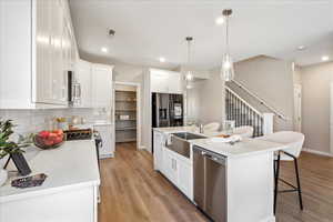 Kitchen with a breakfast bar, appliances with stainless steel finishes, hanging light fixtures, a center island with sink, and light wood-style floors