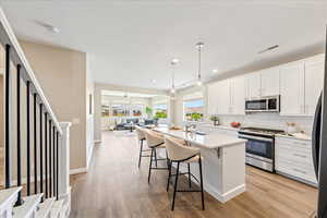Kitchen with appliances with stainless steel finishes, white cabinetry, decorative light fixtures, a kitchen breakfast bar, and recessed lighting