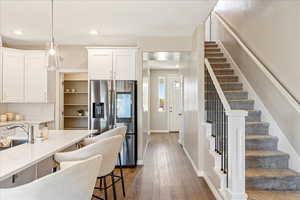 Kitchen featuring stainless steel fridge with ice dispenser, white cabinetry, dark wood-style flooring, hanging light fixtures, and light stone counters