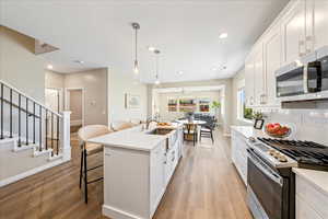 Kitchen featuring white cabinets, stainless steel appliances, a kitchen bar, decorative backsplash, and light wood-style flooring