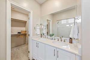 Bathroom with a stall shower, double vanity, light colored carpet, and a walk in closet
