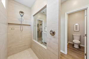 Full bath with wood finished floors, a tile shower, and a spacious closet
