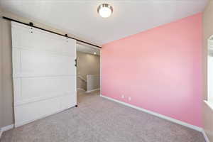 Unfurnished bedroom featuring a barn door and carpet flooring