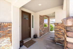 View of exterior entry with brick siding, stucco siding, and covered porch