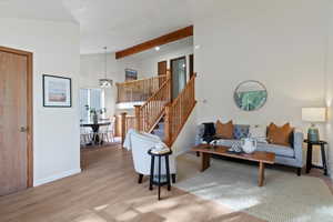 Living area with beamed ceiling, light wood-style flooring, stairway, and high vaulted ceiling