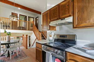 Kitchen with stainless steel range with electric stovetop, hanging light fixtures, under cabinet range hood, light wood finished floors, and beam ceiling