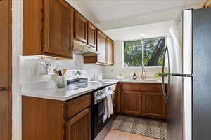 Kitchen with stainless steel appliances, light countertops, brown cabinetry, under cabinet range hood, and light wood finished floors