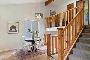 Dining area with light wood finished floors, beamed ceiling, stairway, high vaulted ceiling, and a chandelier