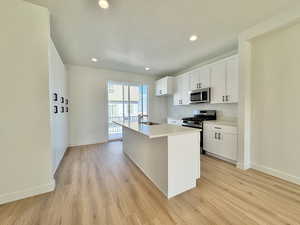 Kitchen featuring appliances with stainless steel finishes, white cabinets, a center island with sink, recessed lighting, and light wood finished floors
