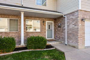 Doorway to property featuring brick siding, a porch, and roof with shingles