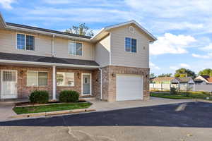 Traditional-style home featuring a porch, brick siding, an attached garage, driveway, and a shingled roof