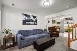 Carpeted living room featuring a textured ceiling, stairs, and ornamental molding